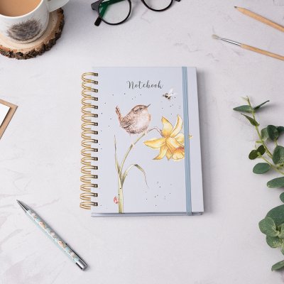 Bird and bee on flower illustration on A5 spiral bound notebook on a desk surrounded by a pen and pencil 