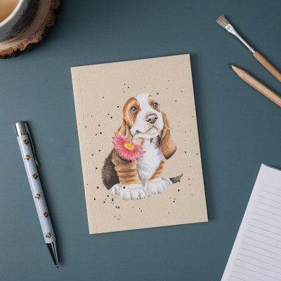 A basset hound puppy holding a flower on an A6 Paperback Notebook