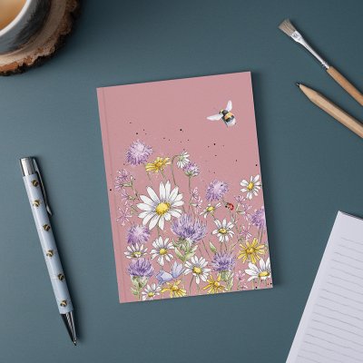 Bee and wild flower illustration on A6 paperback notebook on desk surrounded by a pen and pencil 